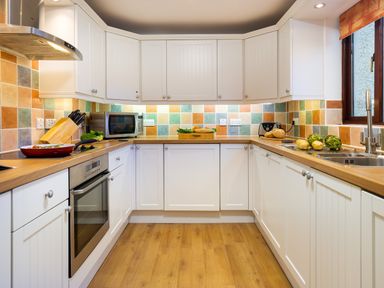 A kitchen with white cabinets wooden countertops tiled backsplash and kitchen appliances at High Lake in Bowness
