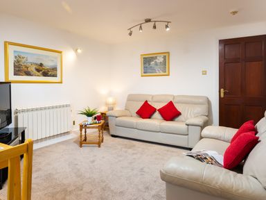 A living room with cream sofas and red cushions a wooden door and framed paintings on the walls at High Lake in Bowness