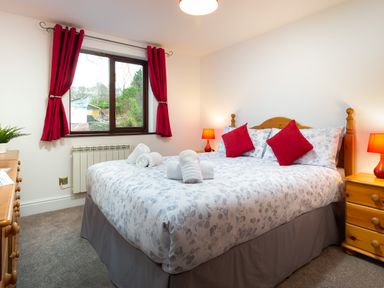 A bedroom with a double bed red pillows red curtains bedside tables with lamps and a window at High Lake in Bowness