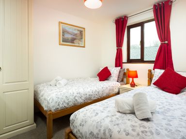 A bedroom with two single beds red curtains and a bedside table with a lamp at High Lake in Bowness