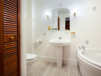 A bathroom with a toilet sink bathtub mirror and wooden louvered door at High Lake in Bowness