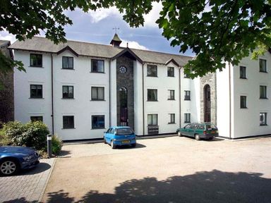 A white multi-story building with cars parked in front and trees casting shadows at High Lake in Bowness