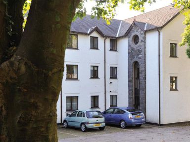 Two cars parked outside a white three-storey building with a stone archway at High Lake in Bowness
