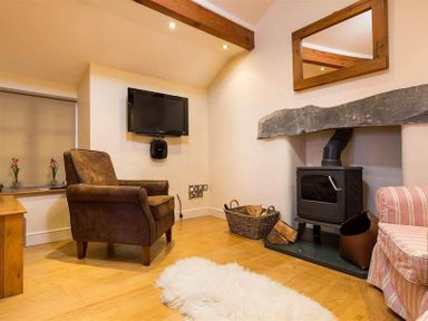 A sitting room with an armchair a wood stove and a TV mounted on the wall at Ivy Cottage in Ambleside