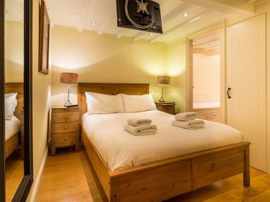 A bedroom with a wooden bed with white bedding and towels on the bed two bedside tables with lamps a wall mirror and a doorway leading to a bathroom at Ivy Cottage in Ambleside