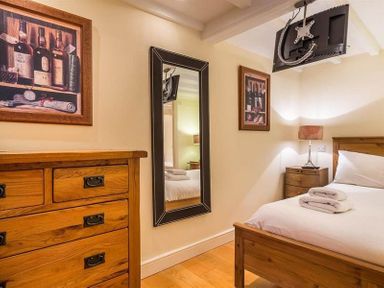 A bedroom with a wooden bed with white bedding and towels a wooden dresser a wall mirror two framed pictures and a TV mounted on the ceiling at Ivy Cottage in Ambleside