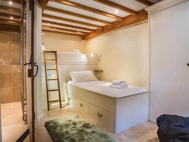 A bedroom with a single bunk bed with ladder a rug and an open door leading to a bathroom at Ivy Cottage in Ambleside