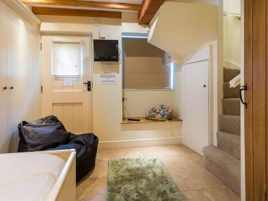 A small room with bean bag chairs a green rug stairs and a wall-mounted television at Ivy Cottage in Ambleside