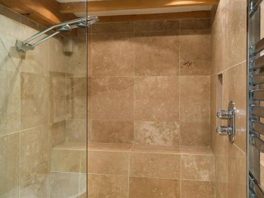 A shower area with tiled walls a glass partition and two chrome knobs at Ivy Cottage in Ambleside