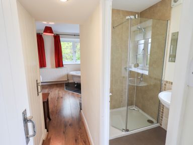 A hallway leading to a bathroom with a shower enclosure and a room with a bathtub and red curtains at The Old Chapel in Crook