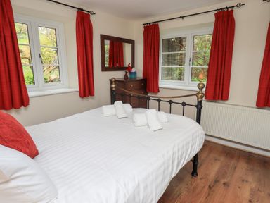 A bedroom with a metal bed white bedding red curtains wooden dresser and two windows at The Old Chapel in Crook