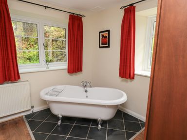 A bathroom with a white clawfoot bathtub red curtains two windows and a wall painting at The Old Chapel in Crook