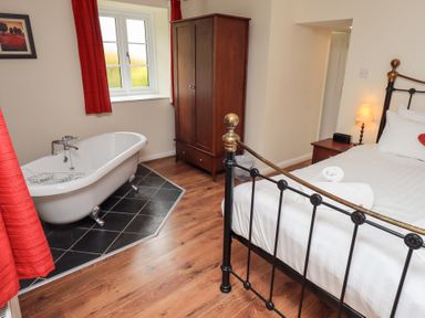 A bedroom with a metal bed frame a wooden wardrobe a bedside table with a lamp and a freestanding bathtub on a tiled floor at The Old Chapel in Crook