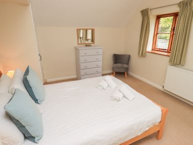 A bedroom with a double bed with pillows and rolled towels a white chest of drawers a mirror a grey chair a window with curtains and a radiator at The Old Chapel in Crook