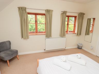 A bedroom with two windows beige curtains a gray chair a mirror and a bed with rolled white towels at The Old Chapel in Crook