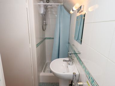 A small bathroom with a shower area with a blue curtain a white sink a mirror and tiled walls at The Old Chapel in Crook