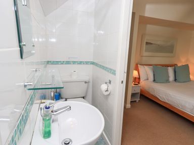 A bathroom with a sink, toilet, and hand soap next to a bedroom with a bed, pillows, nightstand, and lamp at The Old Chapel in Crook