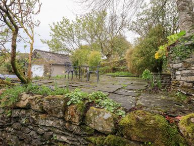 An outdoor stone patio with a metal table and two chairs surrounded by trees and plants at The Old Chapel in Crook