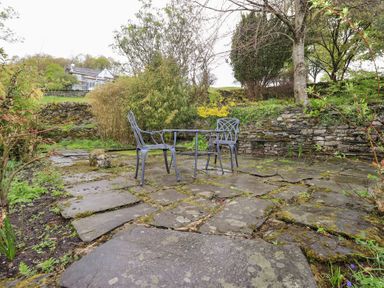 A garden patio area with two metal chairs and a table surrounded by stone walls and trees at The Old Chapel in Crook