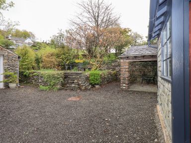 An outdoor area with stone walls a gravel ground trees and metal garden chairs at The Old Chapel in Crook