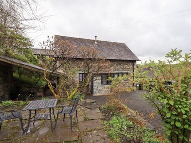 An outdoor patio area with a metal table and chairs in front of a stone building with plants at The Old Chapel in Crook