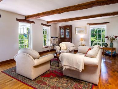 A living room with beige sofas a wooden cabinet a telescope and windows showing greenery at Bank Barn at Rusland Grizedale