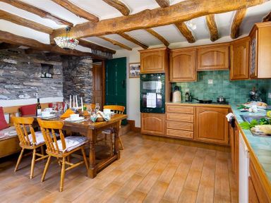 A kitchen with wooden cabinets a dining table with chairs and stone walls at Bank Barn at Rusland in Grizedale