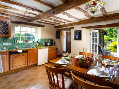 A kitchen and dining area with wooden cabinets a dining table set with tableware and a door leading outside at Bank Barn at Rusland in Grizedale