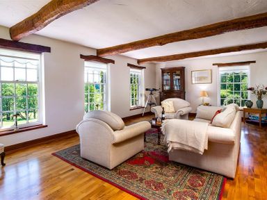 A living room with wooden beams on ceiling armchairs and a sofa around a coffee table on a rug at Bank Barn at Rusland in Grizedale