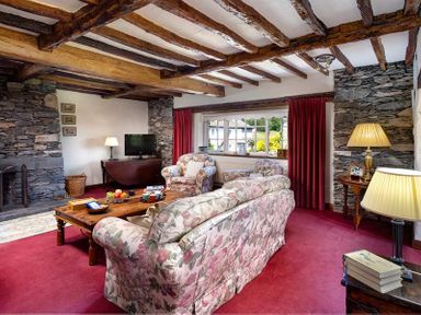 A living room with floral sofas a wooden coffee table stone walls and exposed wooden beams at Bank Barn at Rusland in Grizedale