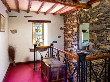 A hallway with exposed wooden beams stone wall stained glass window and wooden chest at Bank Barn at Rusland Grizedale