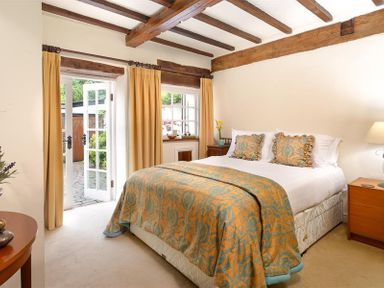A bedroom with a bed covered with a patterned bedspread and pillows next to a window and open French doors with yellow curtains at Bank Barn at Rusland in Grizedale