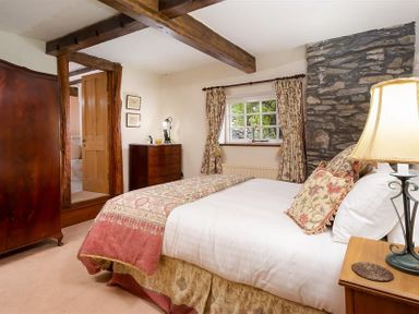 A bedroom with a bed a wooden wardrobe a dresser a window with curtains and exposed wooden beams at Bank Barn at Rusland Grizedale