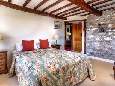 A bedroom with a double bed wooden bedside tables stone wall and exposed wooden ceiling beams at Bank Barn at Rusland in Grizedale