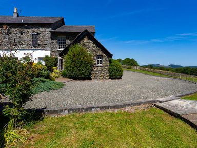 A stone house with a gravel driveway and surrounding greenery at Bank Barn at Rusland in Grizedale