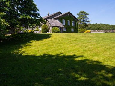 A stone house with ivy on the walls and a large lawn with trees and shrubs at Bank Barn at Rusland in Grizedale
