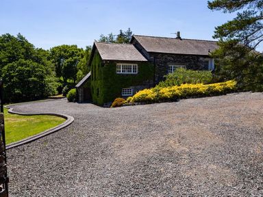 A stone house with a gravel driveway and greenery surrounding it at Bank Barn at Rusland in Grizedale