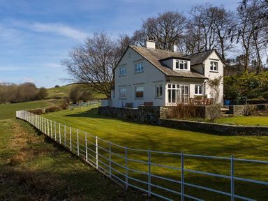 A white house with a fenced lawn and trees in the background at Juniper Cottage in Windermere