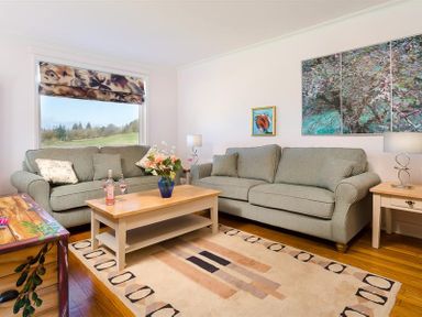 A living room with two gray sofas a wooden coffee table with flowers and wine glasses and large window at Juniper Cottage in Windermere
