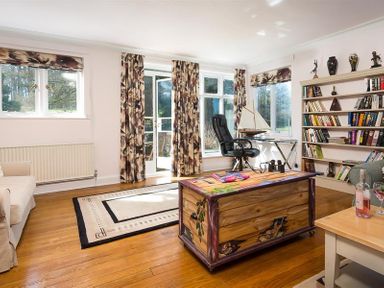 A living room with wooden floors a bookshelf a black office chair and patterned curtains at Juniper Cottage in Windermere
