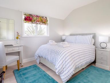 A bedroom with a bed striped bedding and two blue rugs at Juniper Cottage in Windermere