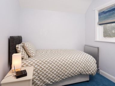 A bedroom with a bed a bedside table with a lamp and radio and a window with a blind at Juniper Cottage in Windermere