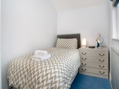 A bedroom with a bed and patterned bedding next to a chest of drawers with a lamp and mirror at Juniper Cottage in Windermere