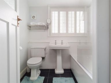 A bathroom with a toilet sink bathtub and window shutters at Juniper Cottage in Windermere