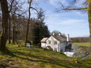 A white house with chimneys surrounded by trees and grassy land at Juniper Cottage in Windermere