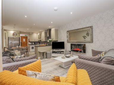 An open plan living room and kitchen with sofas a coffee table a television an electric fireplace and a dining table at Rossett Holme Ambleside