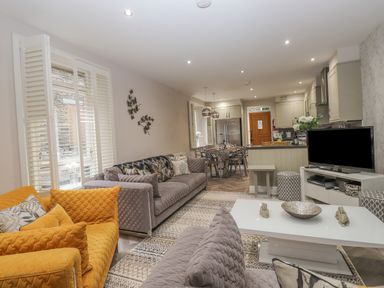 An open living room and kitchen area with sofas, a coffee table, a dining table, a television, and kitchen cabinets at Rossett Holme in Ambleside