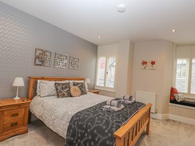 A bedroom with a wooden bed and nightstands and cushions on the window seat at Rossett Holme in Ambleside