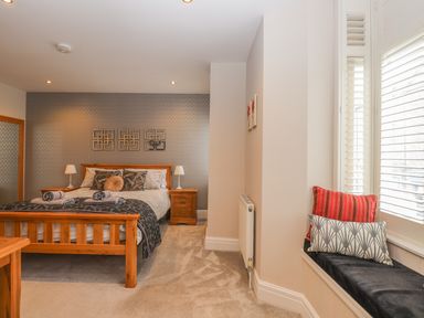 A bedroom with a wooden bed and bedside tables with lamps and a window seat with pillows at Rossett Holme in Ambleside