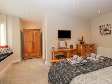 A bedroom with a bed towels wooden wardrobe desk with mirror chest of drawers and wall mounted tv at Rossett Holme in Ambleside